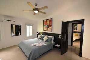 A bedroom with a bed, a ceiling fan, a window, a mirror, and a door leading to another room.