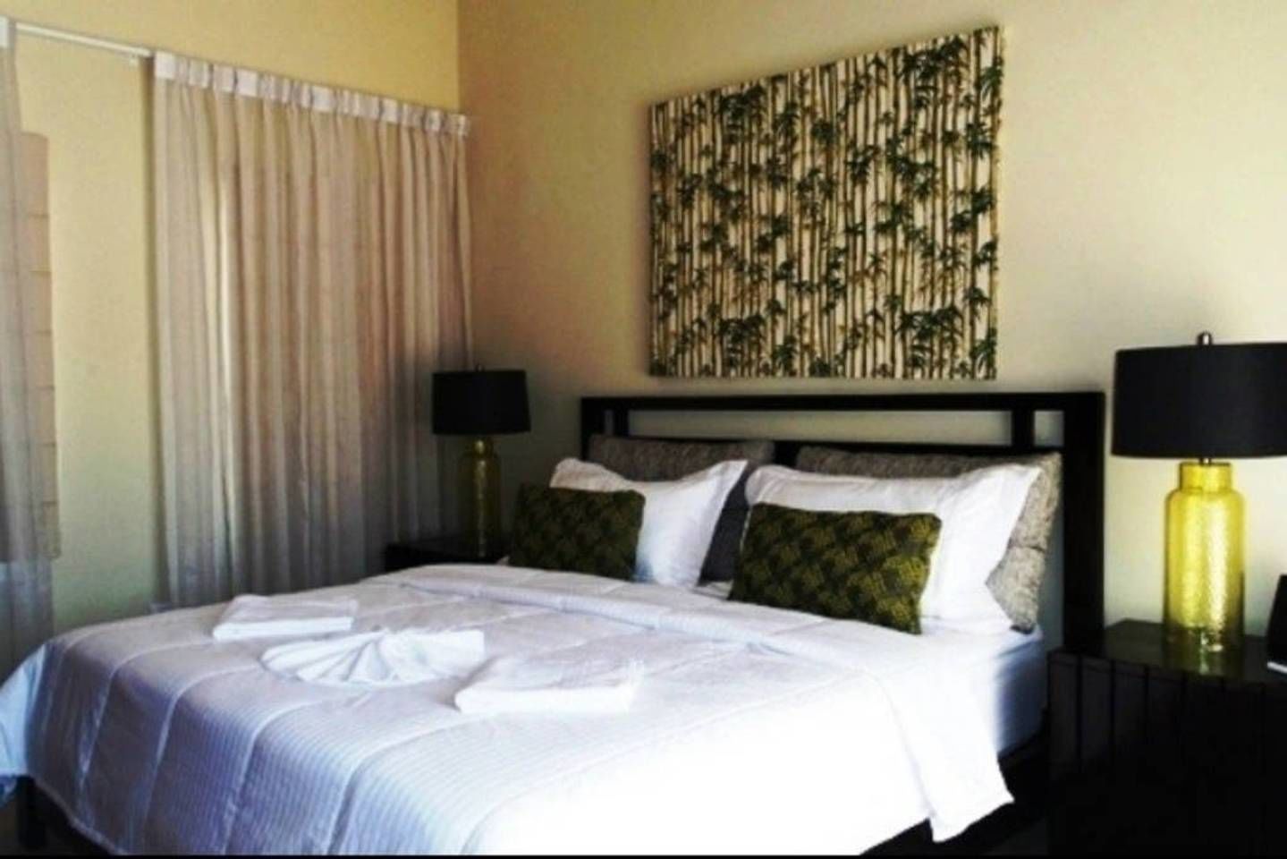 Una habitación de hotel con una cama, una mesita de noche, una lámpara, una cortina y una obra de arte en la pared.