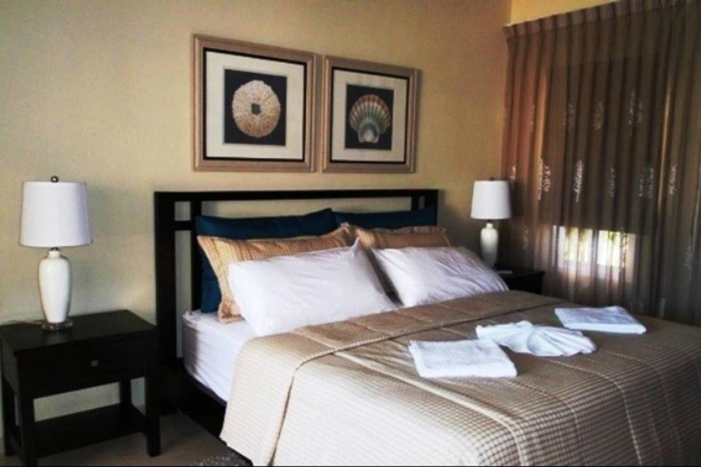 Een hotelkamer met een bed, twee nachtkastjes, twee lampen en twee ingelijste foto's aan de muur.