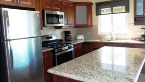A kitchen with wooden cabinets, stainless steel appliances, granite countertops, and a window providing natural light. - Two Bedroom With Jaccuzi Gated (Sosúa)