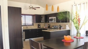 A modern kitchen with dark cabinetry, a central island, and a dining area with a table and chairs. - Villa With Jacuzzi, TVs in all Bedrooms (Sosúa)