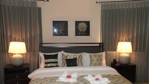 Une chambre d’hôtel avec un lit, deux tables de chevet, deux lampes et deux tableaux encadrés au mur.