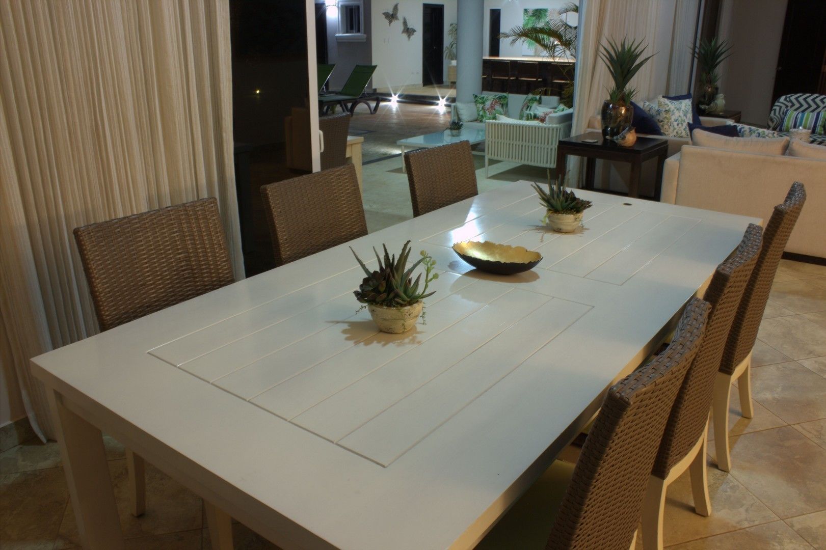 Een eetgedeelte met een witte tafel, rieten stoelen en potplanten.