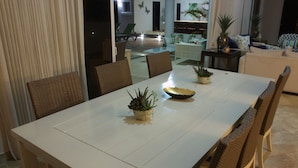 Un coin repas avec une table blanche, des chaises en osier et des plantes en pot.