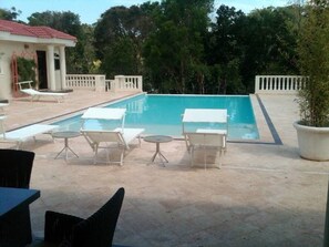 A swimming pool with lounge chairs and tables, surrounded by a white fence and trees. - Touch of Elegance! 6 Bedroom Near the Beach (Sosúa)