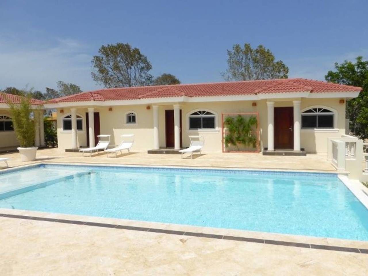 A poolside view of a two-story building with a red-tiled roof, white columns, and a swimming pool.