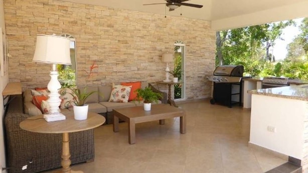 Un vaste espace patio agrémenté d’un mur en pierre, d’un ventilateur de plafond, d’une table à manger, d’un canapé et d’un coin barbecue.