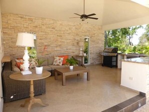 Un vaste espace patio agrémenté d’un mur en pierre, d’un ventilateur de plafond, d’une table à manger, d’un canapé et d’un coin barbecue.