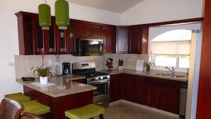 Une cuisine avec des meubles en bois foncé, un îlot central doté de tabourets, un four à micro-ondes, une cuisinière et un évier.