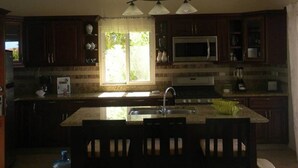 A kitchen with dark wooden cabinets, a stainless steel sink, a microwave, and a large window with natural light. - Villa in Gated Community Furnished Lots Amenities (Sosúa)