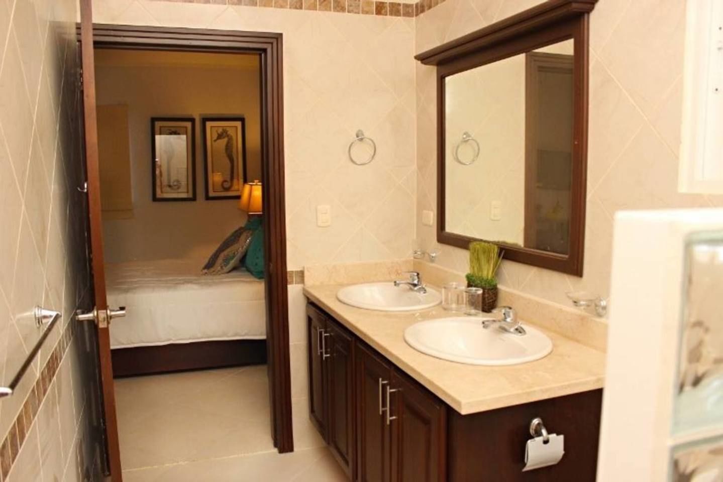 A bathroom with two sinks, a mirror, and a bed visible through an open door.