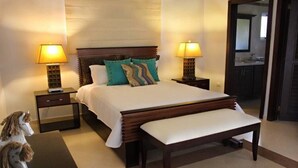 Habitación de hotel impecable con una cama grande, dos mesitas de noche con lámparas, un banco y una pequeña estatua de un caballo.