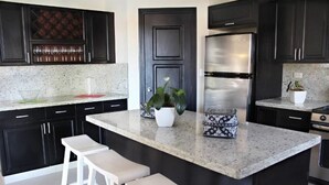 Una cocina moderna con armarios oscuros, un refrigerador de acero inoxidable, encimera de granito y una planta en maceta.
