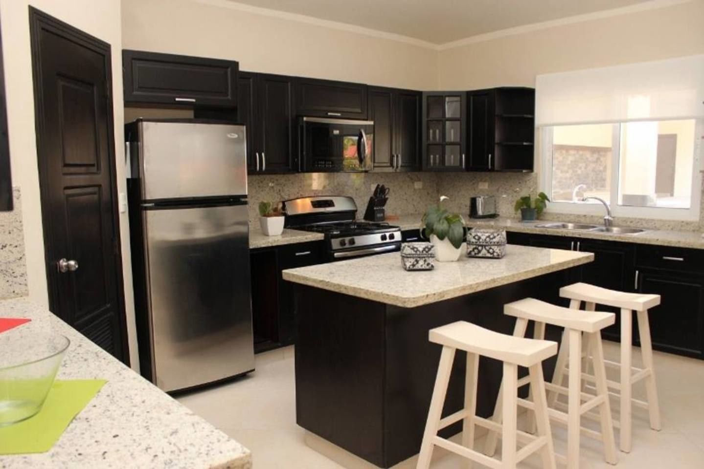 A modern kitchen with dark cabinets, stainless steel appliances, a granite countertop, and a central island with bar stools.