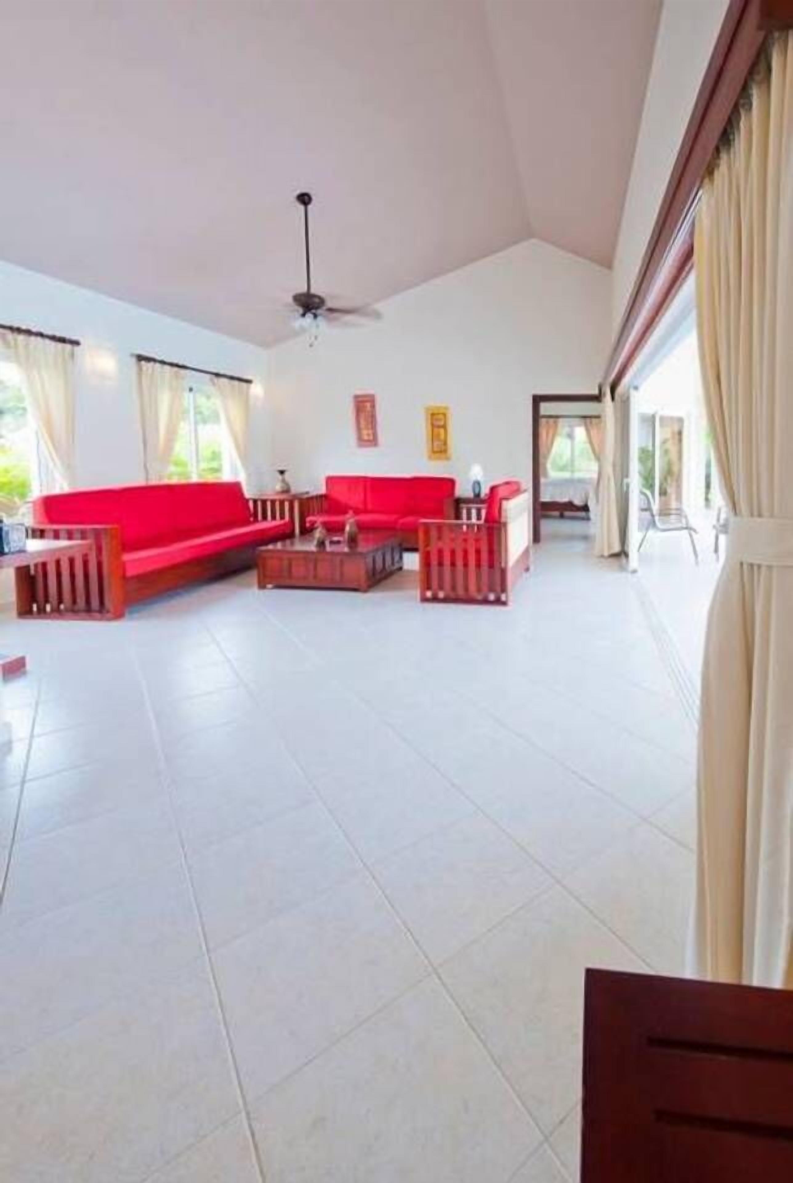 A spacious living area with a red sofa set, a coffee table, and a ceiling fan.