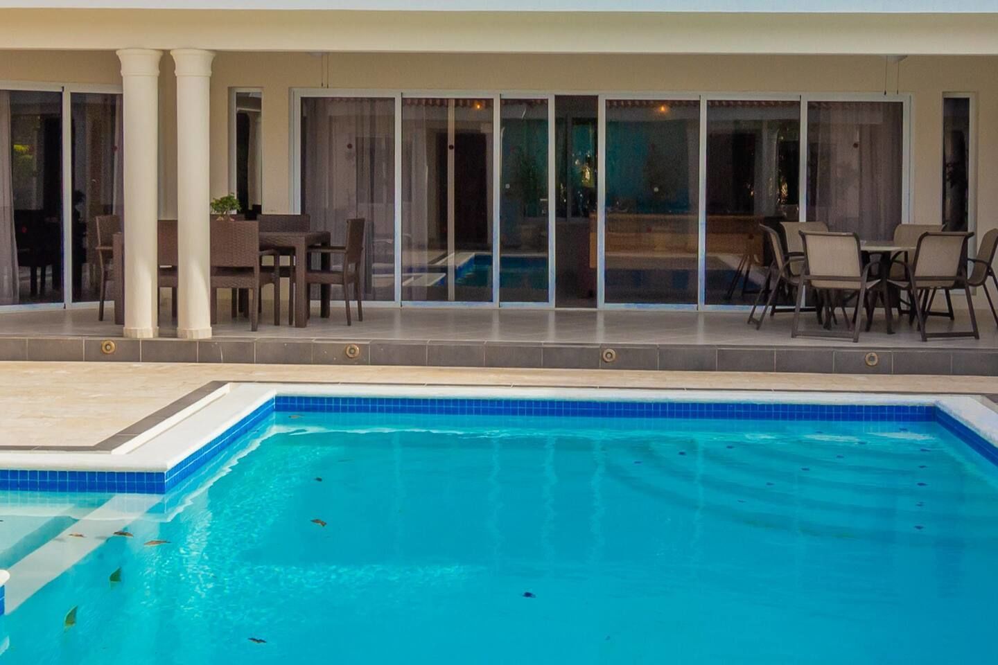 Piscina com deck revestido, cercada por mobiliário de exterior e um espaço coberto de varanda.