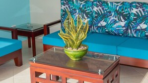 A modern living room with a glass-top coffee table, a green plant, and a blue sofa with a tropical leaf pattern. - Privacy and Comfort Luxury 6 Bedroom Villa (Sosúa)