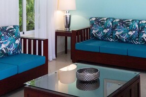 A living room with a glass coffee table, two sofas with patterned cushions, a small side table with a lamp, and a view of greenery through a window. - Privacy and Comfort Luxury 6 Bedroom Villa (Sosúa)
