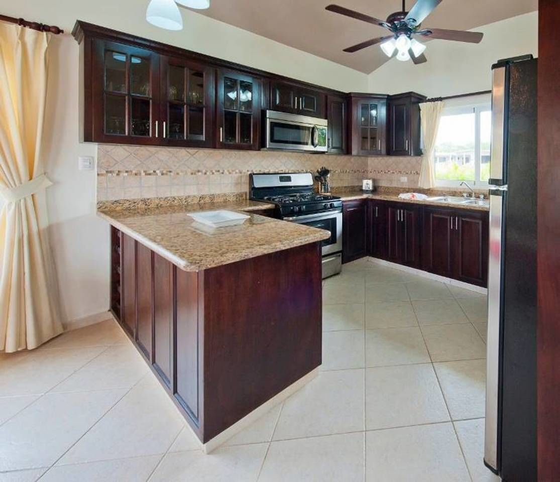 A kitchen with dark wooden cabinets, a granite countertop, a microwave, an oven, and a ceiling fan.
