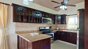 A kitchen with dark wooden cabinets, a granite countertop, a microwave, an oven, and a ceiling fan. - Privacy and Comfort Luxury 6 Bedroom Villa (Sosúa)