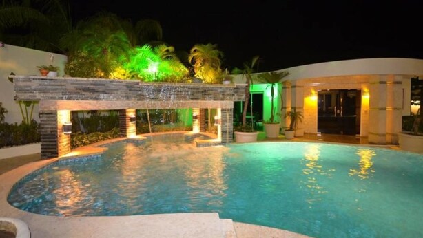 Un área de piscina nocturna con una estructura de piedra e iluminación verde.