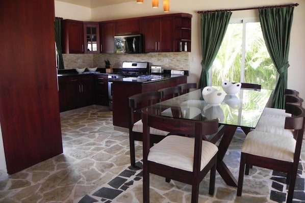 A kitchen with dark wooden cabinets, a central island, and a dining area with a glass table and chairs.