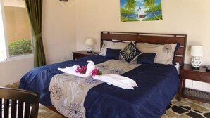 Een net opgemaakt bed met een blauwe en witte bloemenbedekking, een paar witte handdoeken met bloemen, en een schilderij van een strandgezicht aan de muur.