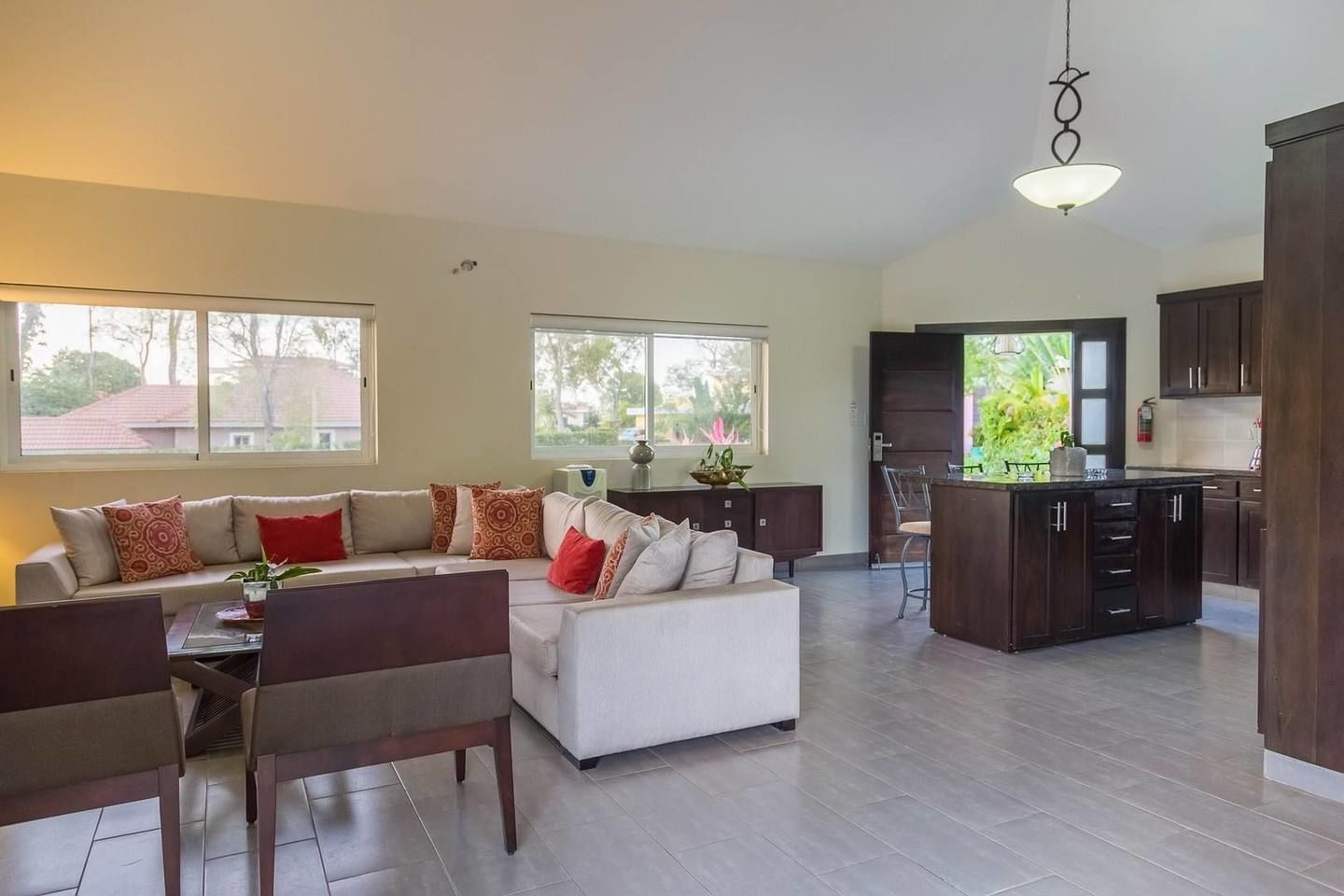 Amplia sala de estar con sofá, mesa de comedor y cocina con armarios oscuros y una isla grande.