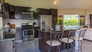 A modern kitchen with dark wood cabinets, stainless steel appliances, and a central island with bar stools. - Villa Equipped With an Infinity Edged Pool in Gated Community (Sosúa)