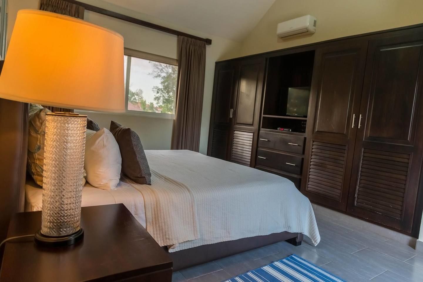 Un dormitorio con cama, mesita de noche, lámpara, ventana y armario.