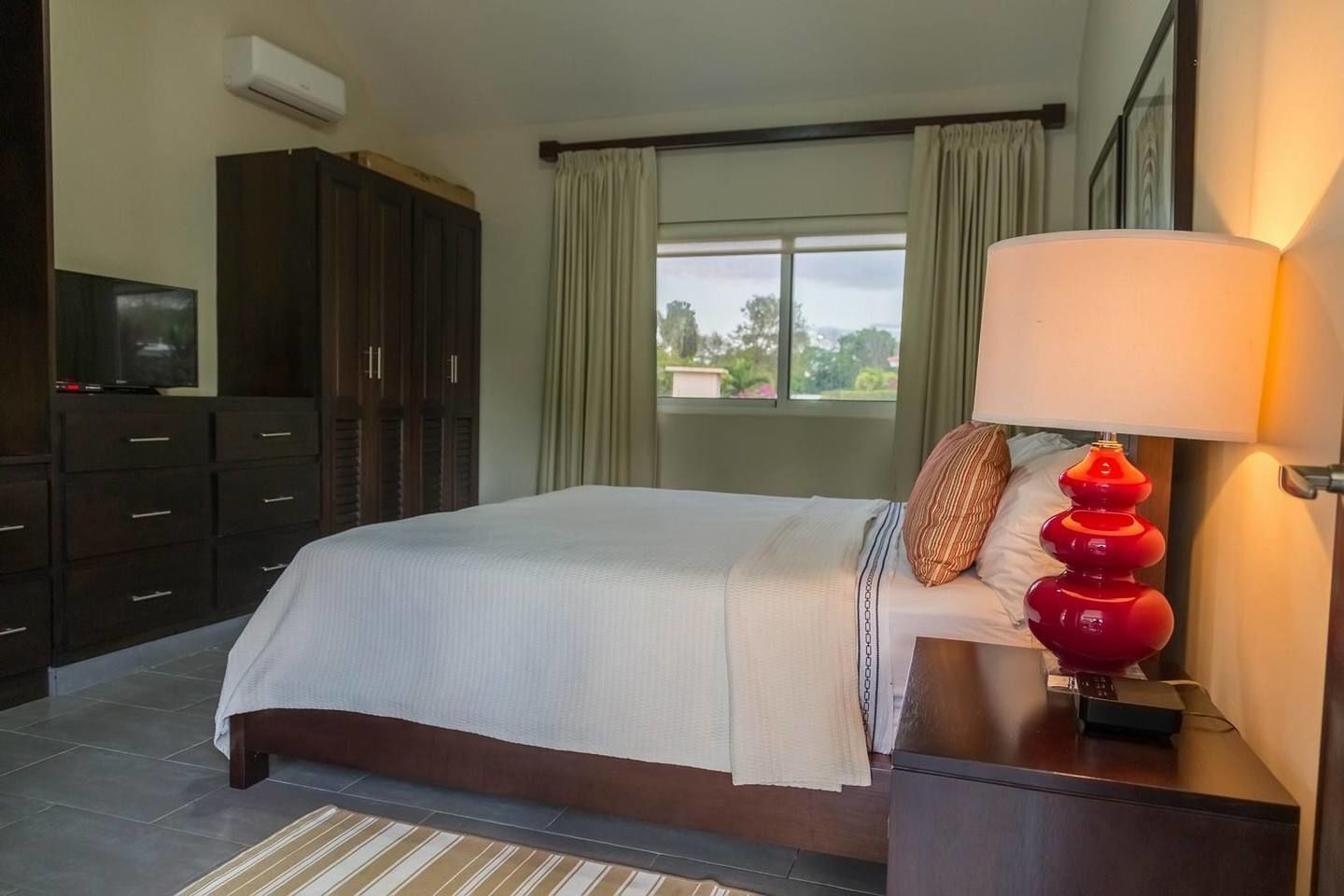 A hotel room with a bed, a TV, a lamp, and a window with curtains.