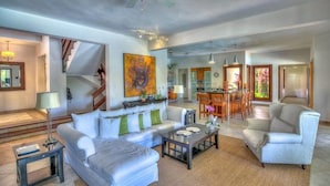 A spacious living area with a sofa, armchairs, and a coffee table. There is a staircase leading to an upper level, a dining area with chairs, and a kitchen in the background. - Villa Jardin Paraiso Cabarete Villa Near the Beach (Cabarete)