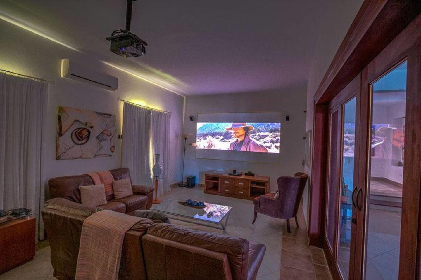 Ein Wohnzimmer mit großem Fernseher, einer Couch, einem Sessel und einem Couchtisch.