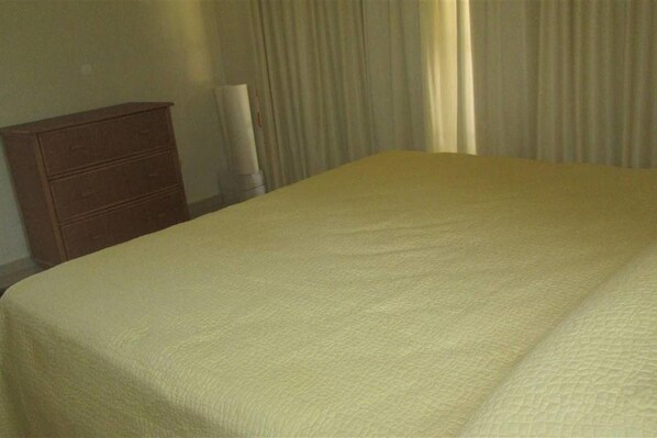 A hotel room with a bed, a wooden dresser, and a lamp.