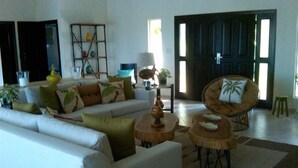 Un salón con un sofá, dos mesas redondas y una silla. Se ve una puerta al fondo.
