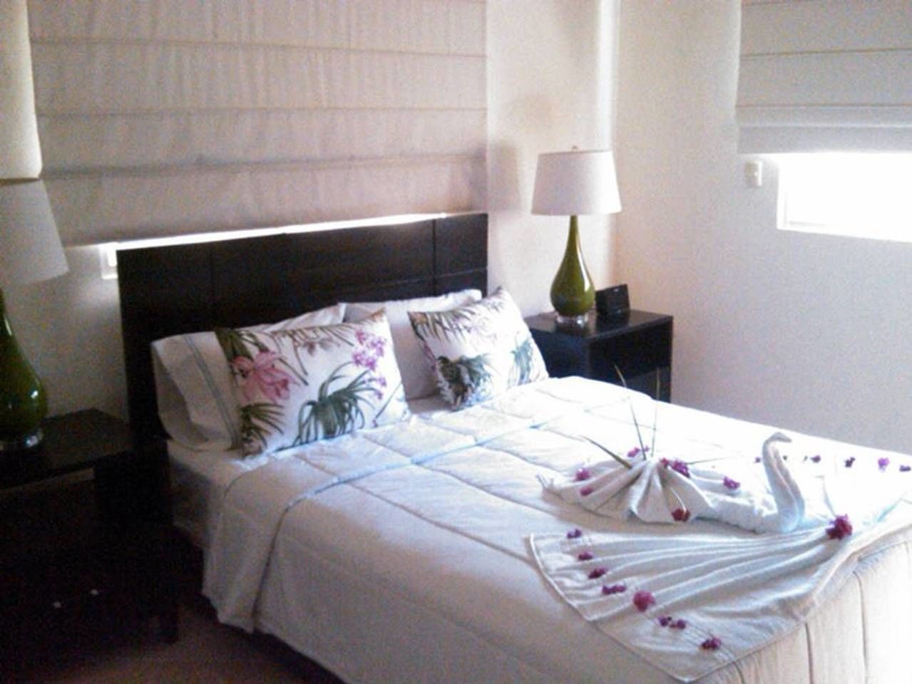 A neatly made bed with floral pillows, a decorative swan, and a green vase on a bedside table.