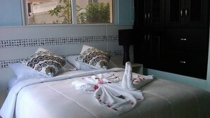 Habitación de hotel con dos camas, cada una con ropa blanca y almohadas estampadas. Amplia ventana con vista a zonas verdes.
