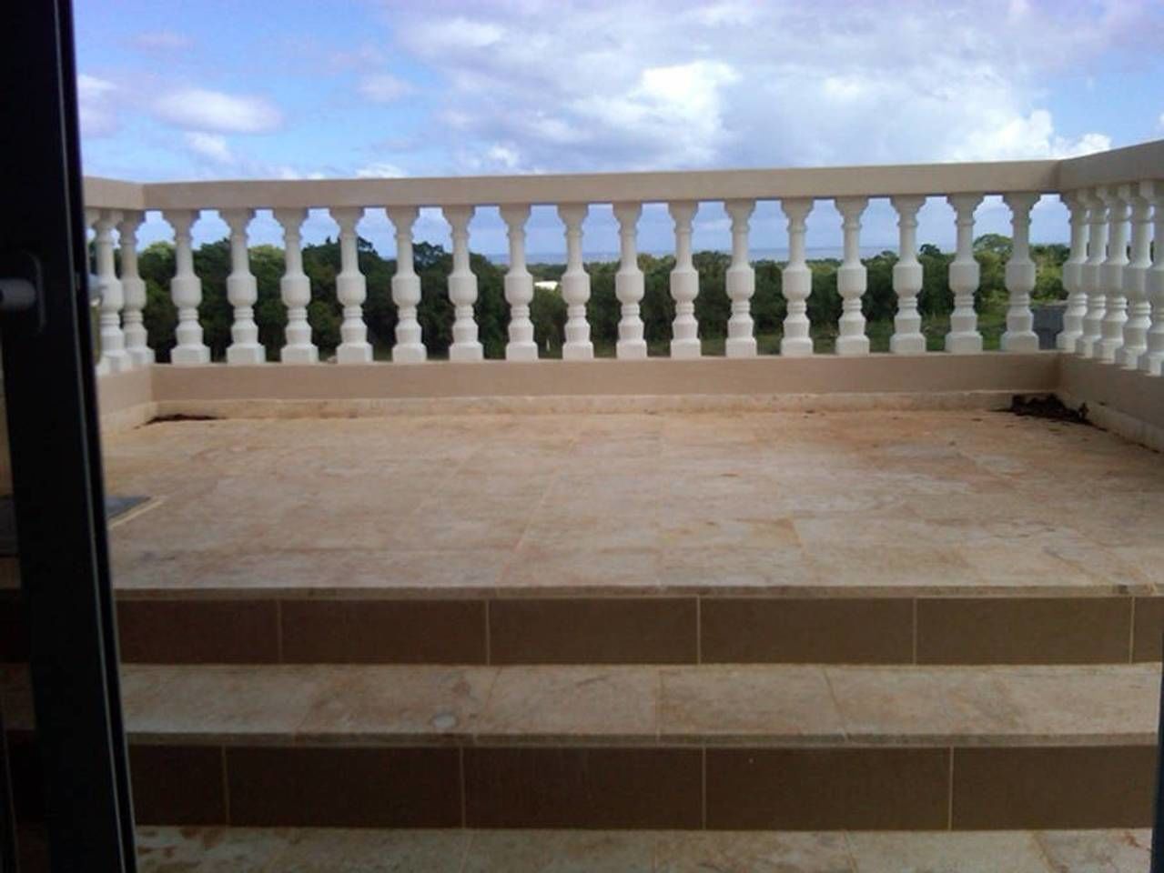 A balcony with a white balustrade and a view of the sky and trees.