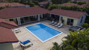 Une grande piscine avec des chaises longues, entourée d’un patio couvert doté d’un toit en tuiles.
