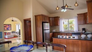 Une cuisine moderne avec des meubles en bois, un réfrigérateur en acier inoxydable et un coin repas comprenant une table et des chaises en verre.