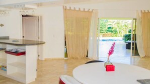 A modern kitchen with a built-in island, a dining area with a round table, and a view of a pool and greenery outside. - Private Villa With Pool in Sosua for Large Groups (Sosúa)
