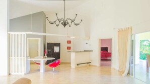 A spacious living area with a modern kitchen, a dining table with red chairs, and a large window offering a view of greenery. - Private Villa With Pool in Sosua for Large Groups (Sosúa)