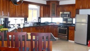 Une cuisine moderne avec des meubles en bois, un îlot central, des appareils électroménagers en acier inoxydable et un coin repas avec des chaises en bois.