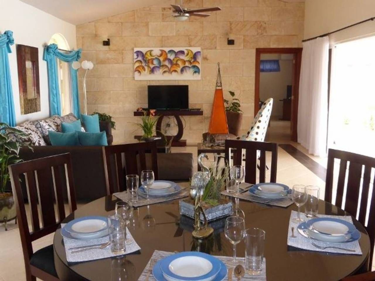 Un coin repas avec un mur en pierre, un téléviseur et une table à manger dressée pour six personnes.