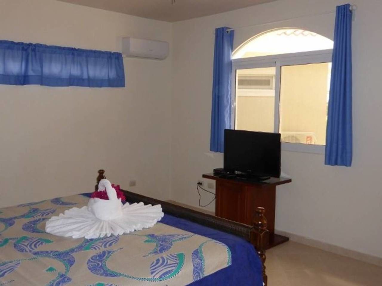 A hotel room with a bed, a television on a wooden stand, and a window with curtains.