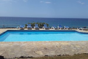 A swimming pool with lounge chairs and a view of the ocean.