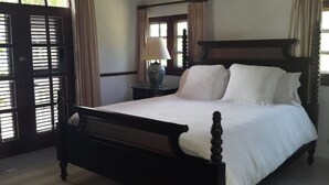 A traditional bed with a wooden frame and white bedding, a bedside table with a lamp, and a window with curtains. - Spacious Oceanfront Villa (Sosúa)