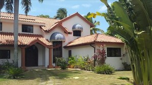 A two-story house with a tiled roof, a covered porch, and a well-maintained lawn. - Spacious Oceanfront Villa (Sosúa)