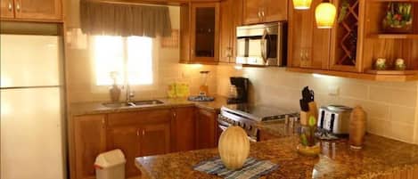 A kitchen with wooden cabinets, a granite countertop, a refrigerator, a microwave, a stove, and pendant lights.