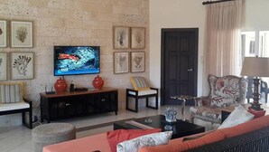 Sala de estar com parede de pedra, televisão, obras de arte emolduradas, sofá, poltrona e mesa de centro.